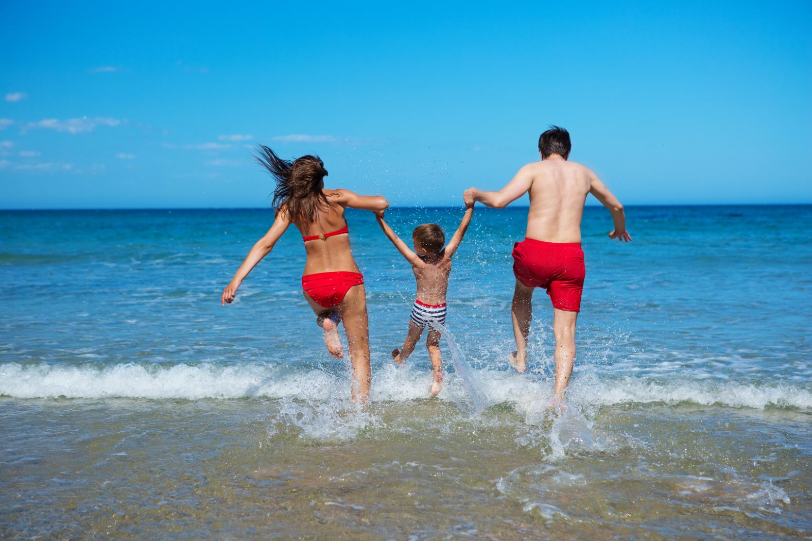 Family running into the sea on a sunny beach during a summer holiday in Greece