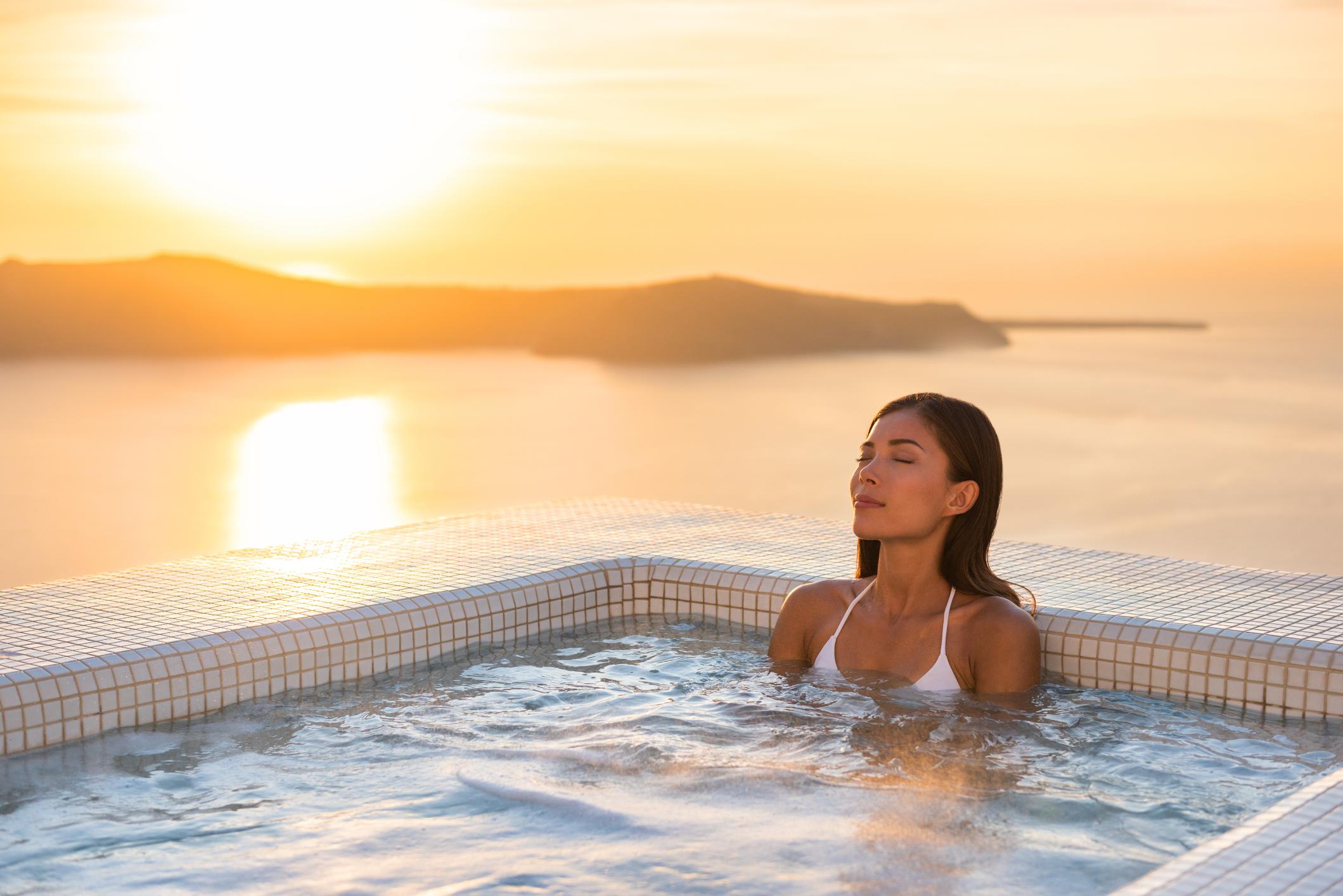 Woman relaxing in luxury spa jacuzzi with sea sunset view in Greece