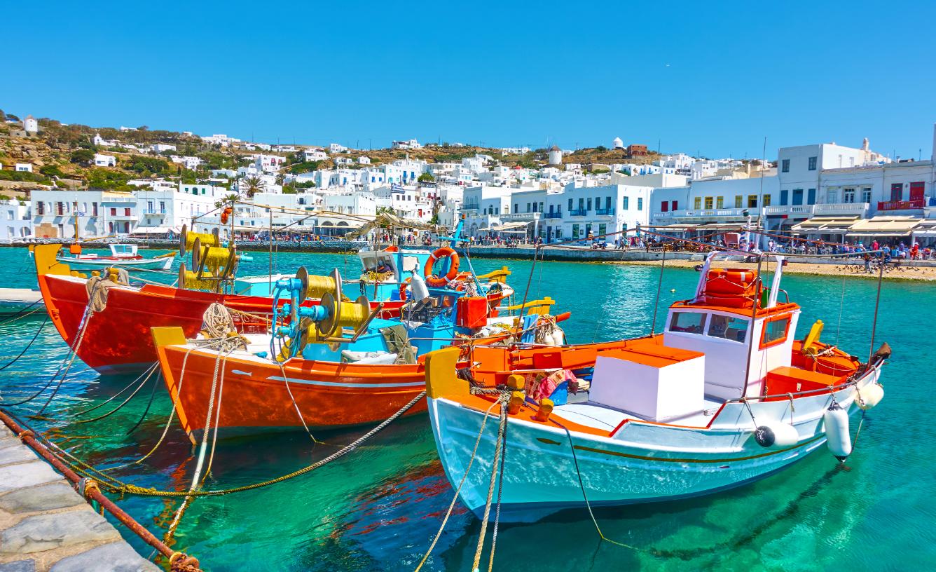 Colorful fishing boats in Mykonos harbor with white Cycladic houses, Greece