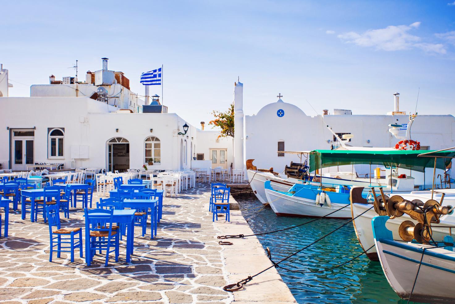 Traditional seaside taverna with blue chairs and fishing boats in Paros harbor, Greece