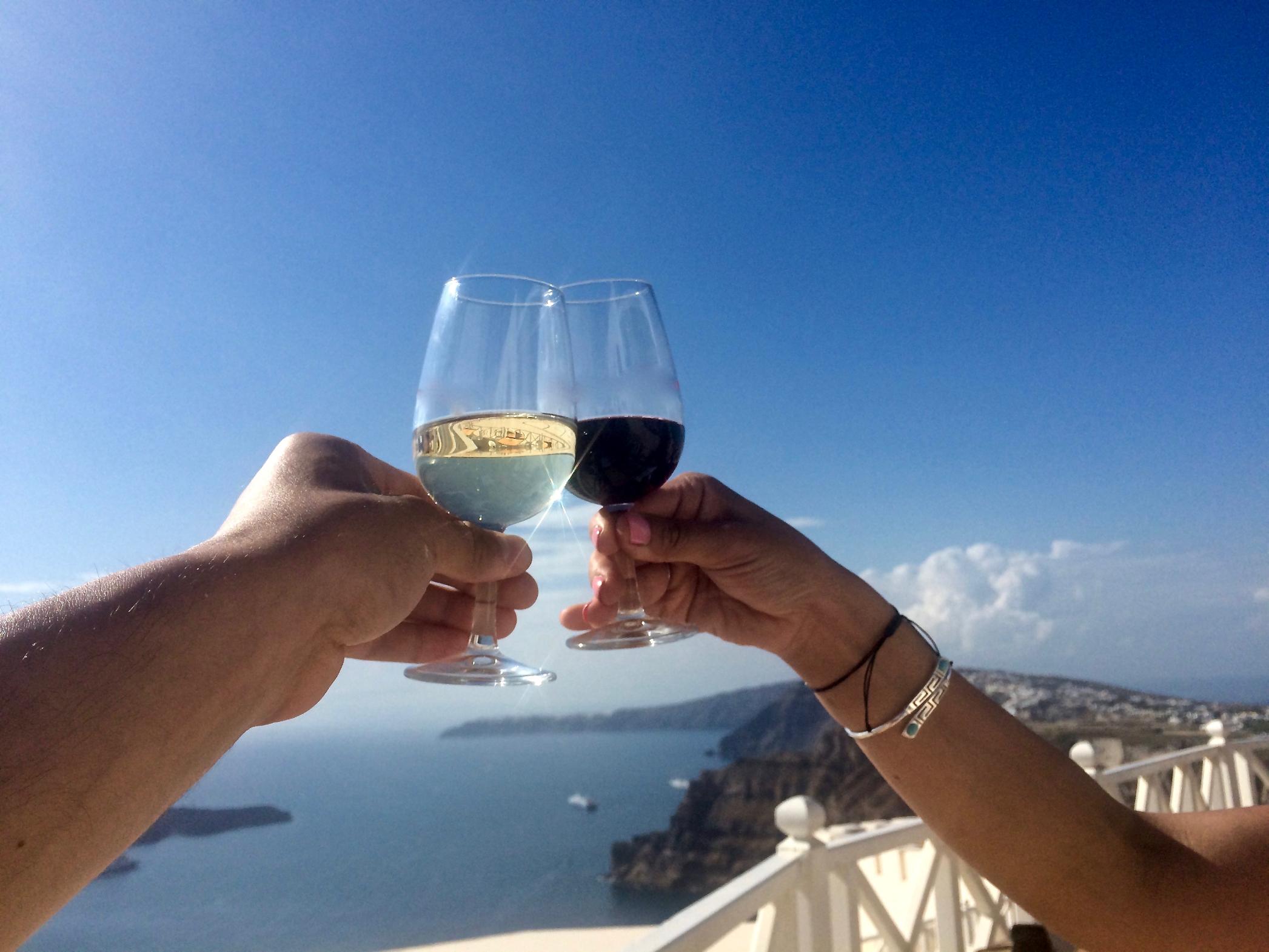 Couple toasting wine glasses overlooking the Santorini caldera and Aegean Sea, Greece