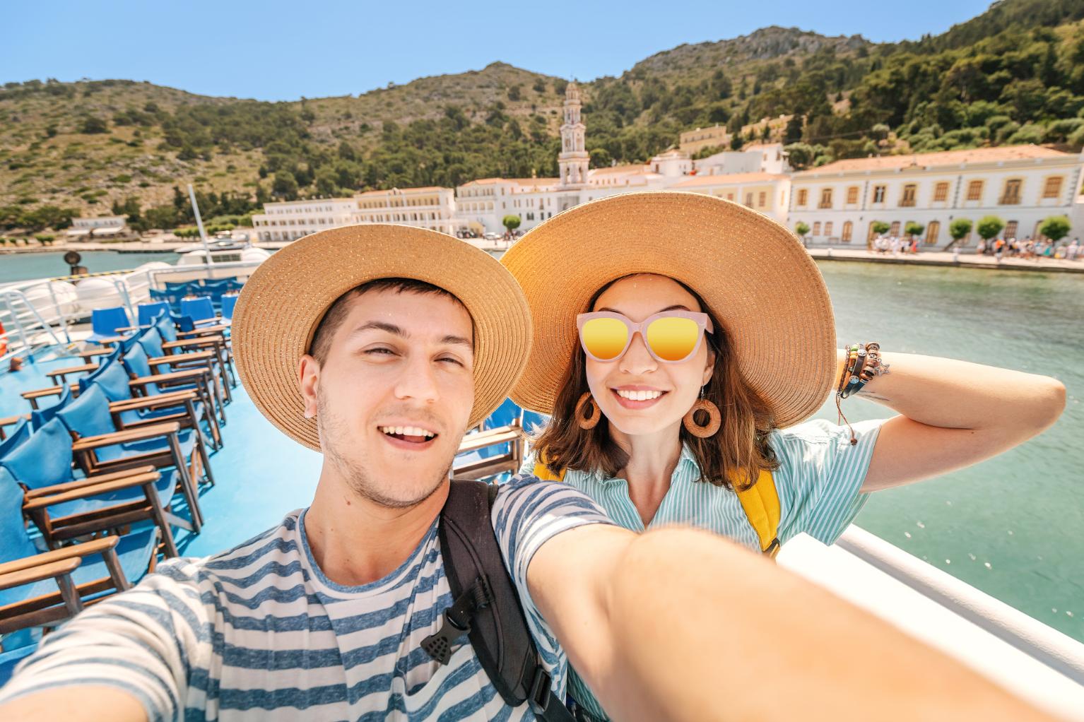 Couple taking a selfie while arriving by boat at Symi Island harbor in the Dodecanese, Greece